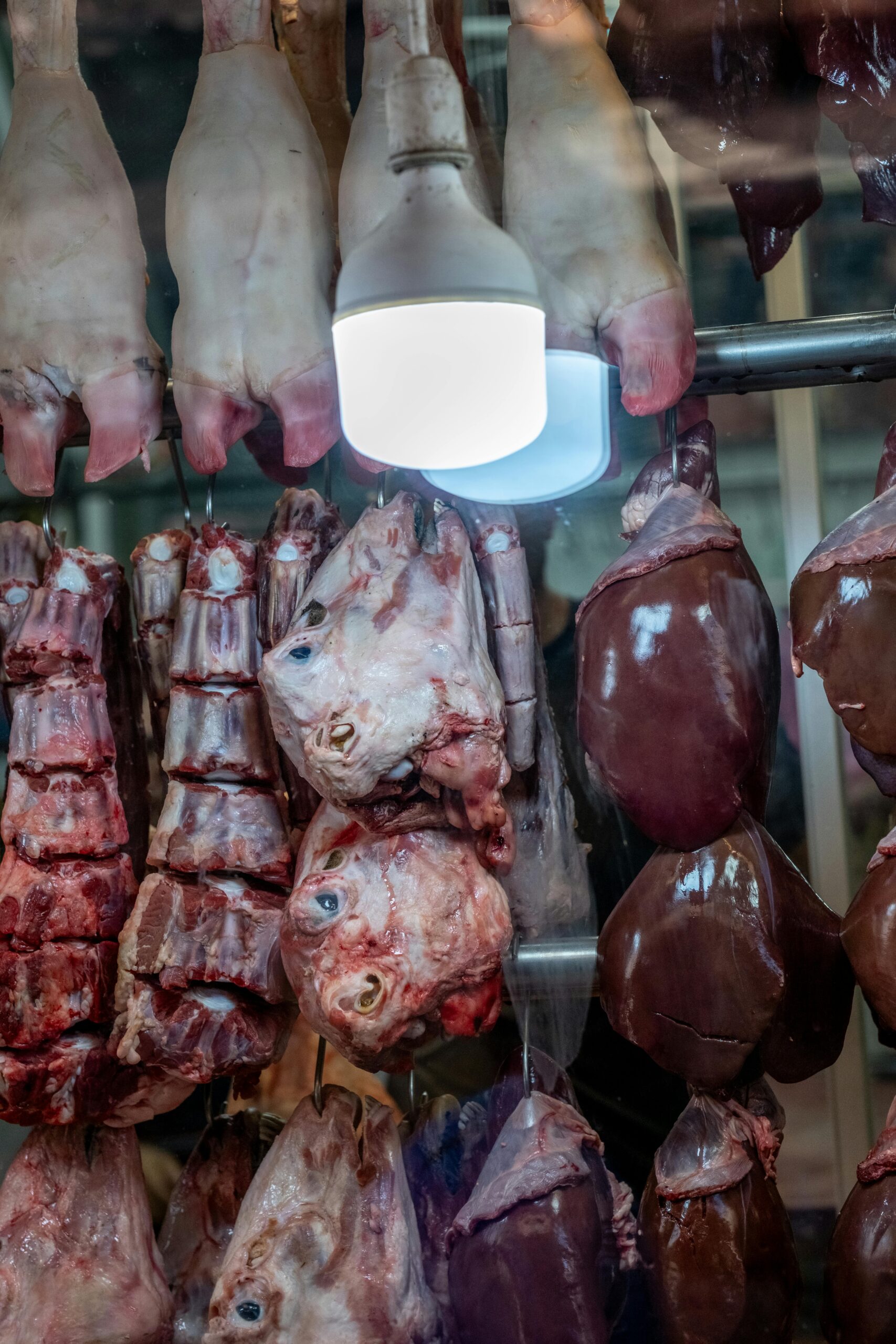 Detailed view of hanging meat cuts in a butchery in İzmir, Türkiye, showcasing diverse animal parts under lamp lighting.