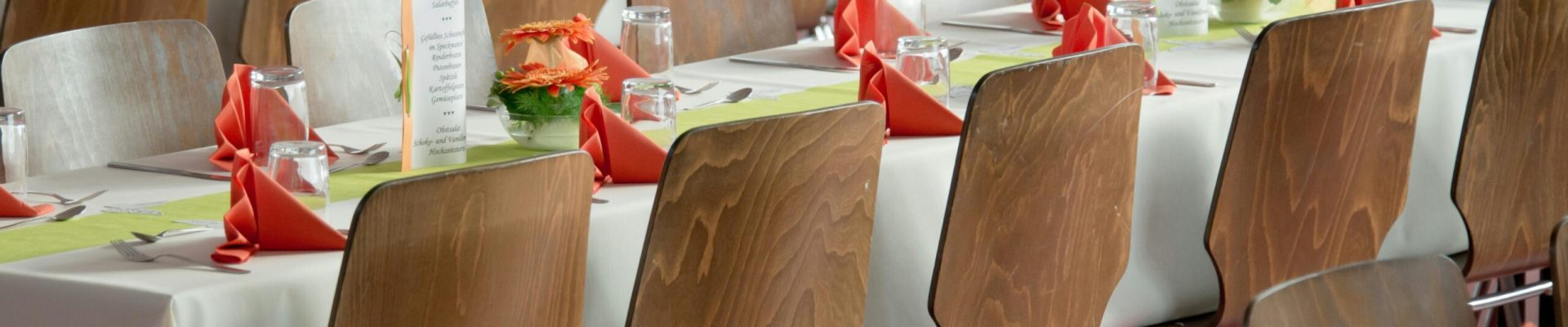 Beautifully arranged tables with wooden chairs for a formal event, adorned with orange flowers.